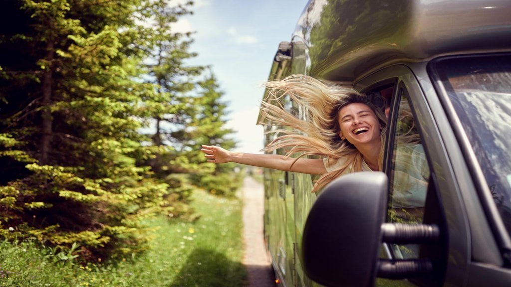 Blonde woman on the window of an RV with hands out smiling enjoying ride.Transport, roadtrip, nature concept. 