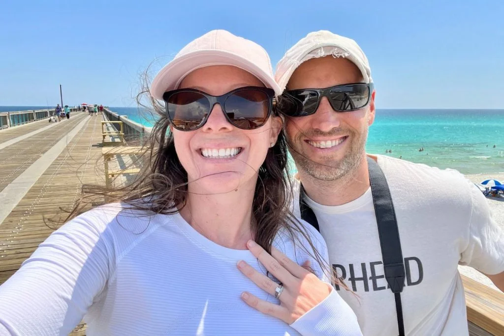Ashlee and Pablo smiling along a pier with the ocean in the background in Florida.